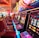 A brightly lit casino interior featuring a row of colorful slot machines. The neon lights create a vibrant atmosphere, with patterned carpeting adding to the decor. Stools are aligned neatly in front of each machine.
